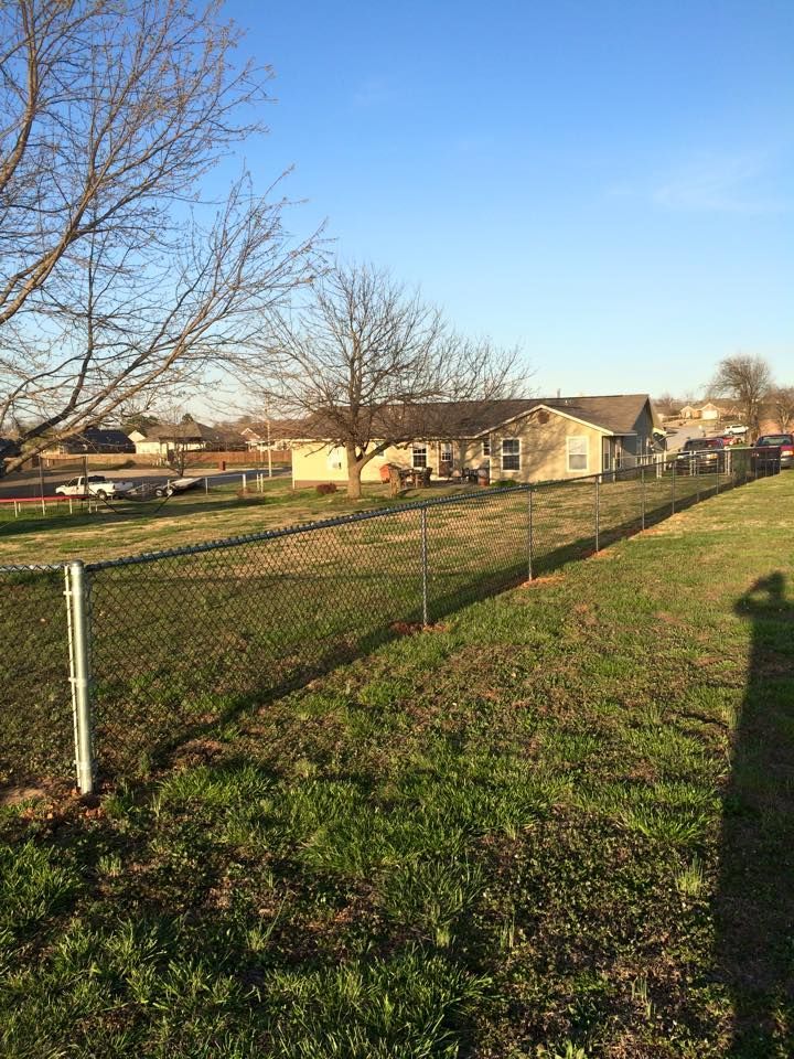 A chain link fence surrounds a grassy field with a house in the background.
