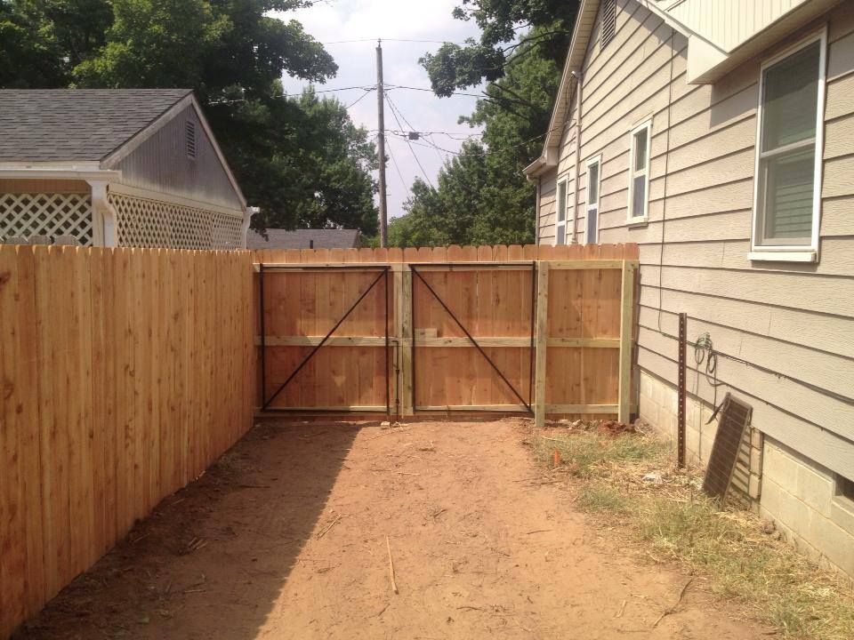 A wooden fence surrounds a dirt road leading to a house