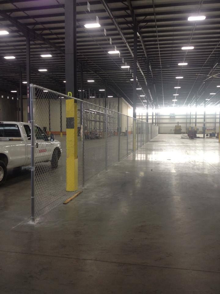 A truck is parked in a large warehouse behind a chain link fence.