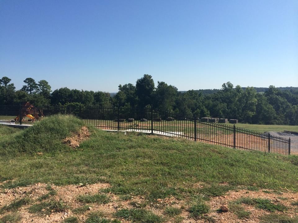 A fence surrounds a grassy field with trees in the background