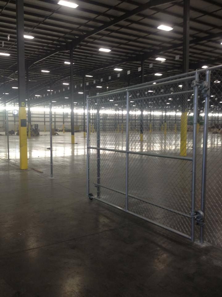 There is a chain link fence in the middle of a large warehouse.