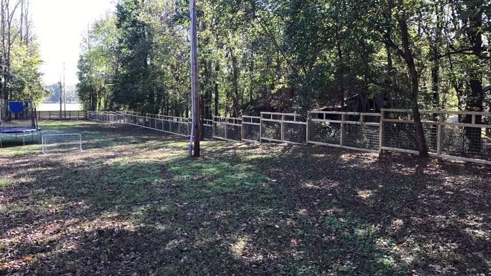 There is a chain link fence in the middle of a field surrounded by trees.