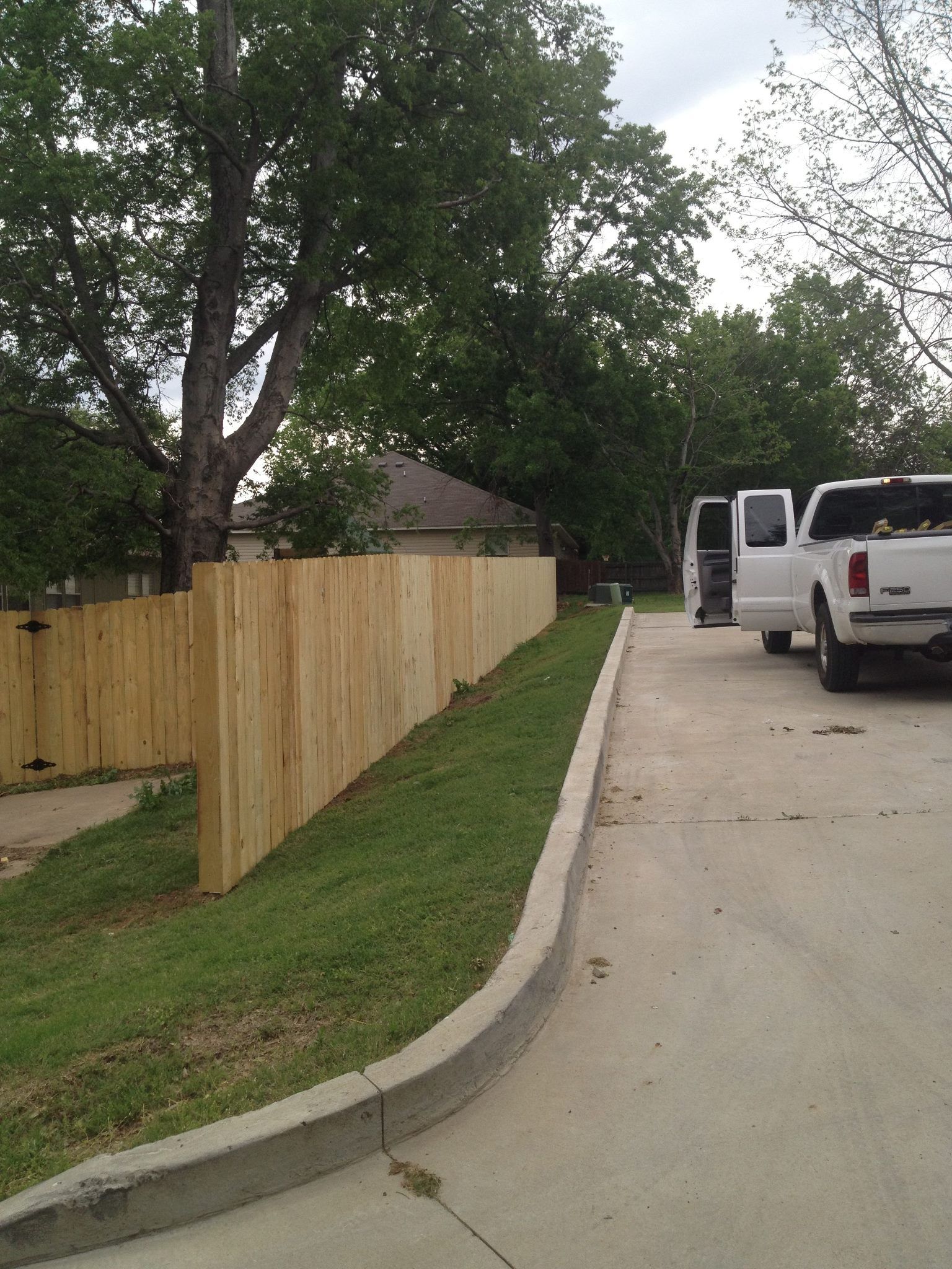 A white truck is parked on the side of the road next to a wooden fence.
