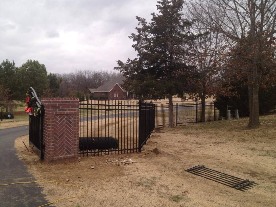 A black fence surrounds a brick pillar in a field