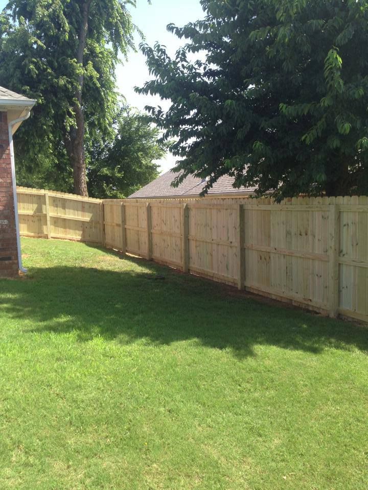 A wooden fence surrounds a lush green lawn in a backyard.