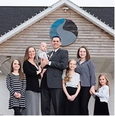 Family poses in front of a building with a blue and gray logo.