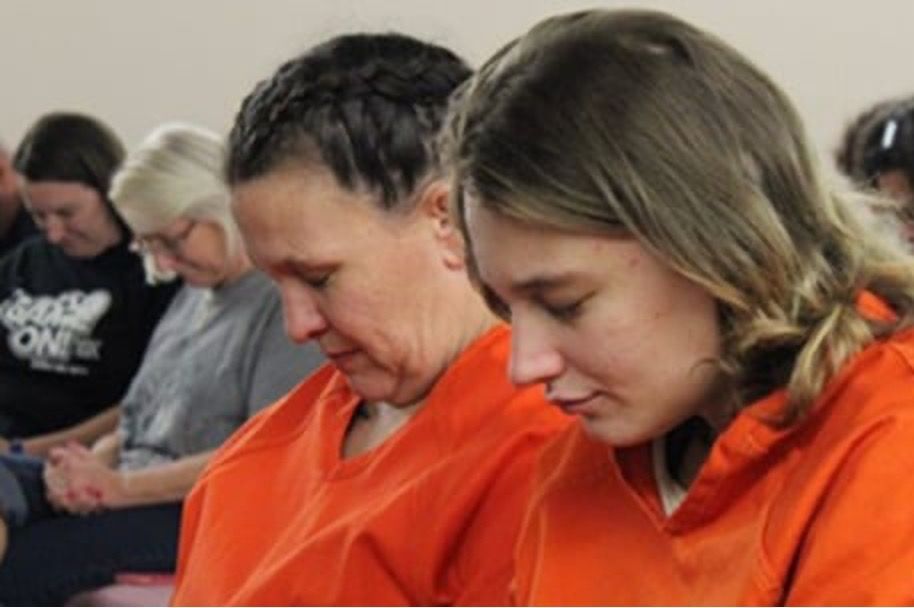 People in orange jumpsuits and other individuals praying, heads bowed.