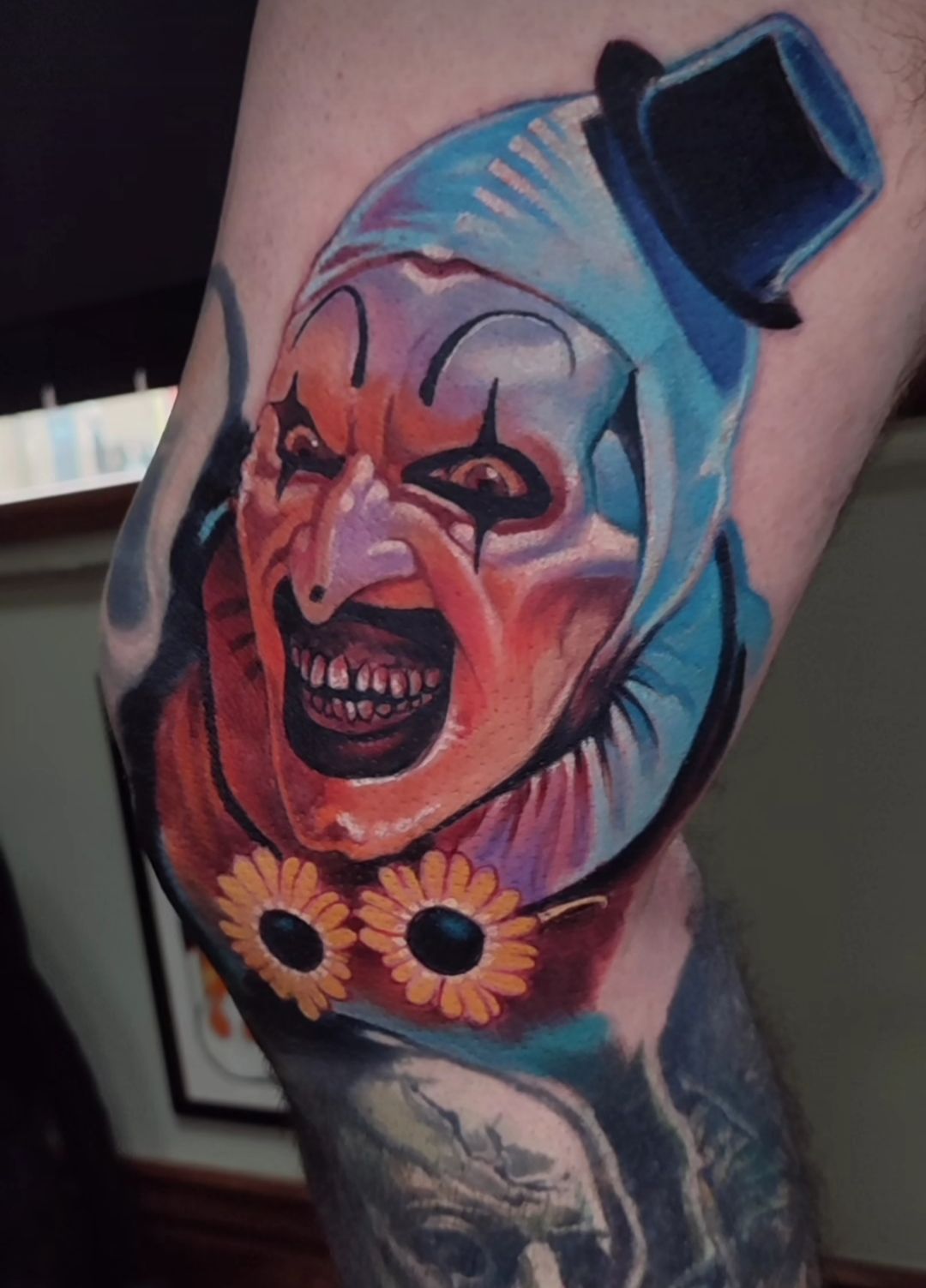 A grotesque clown tattoo on a leg, with a top hat, sunflower glasses, and a sinister grin.