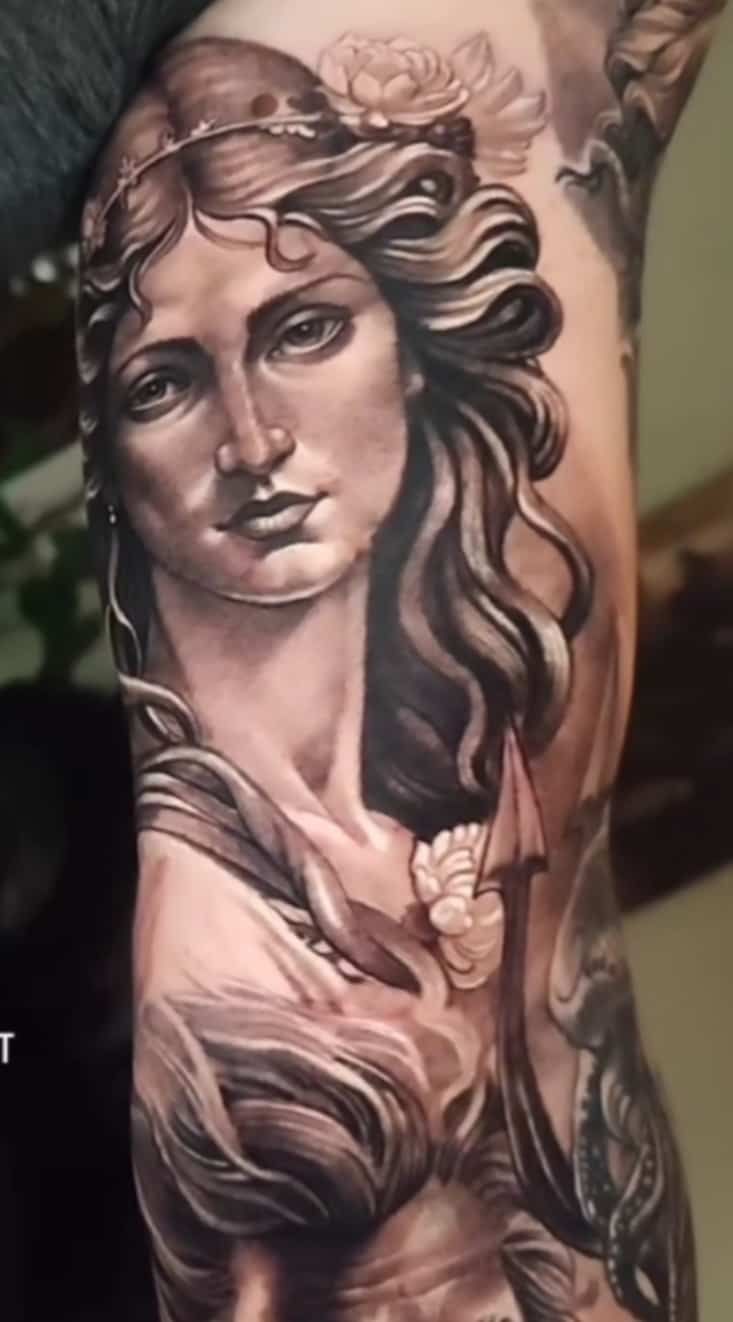 Tattoo of a woman's bust, with flowing hair, floral crown, and intricate details on an arm.