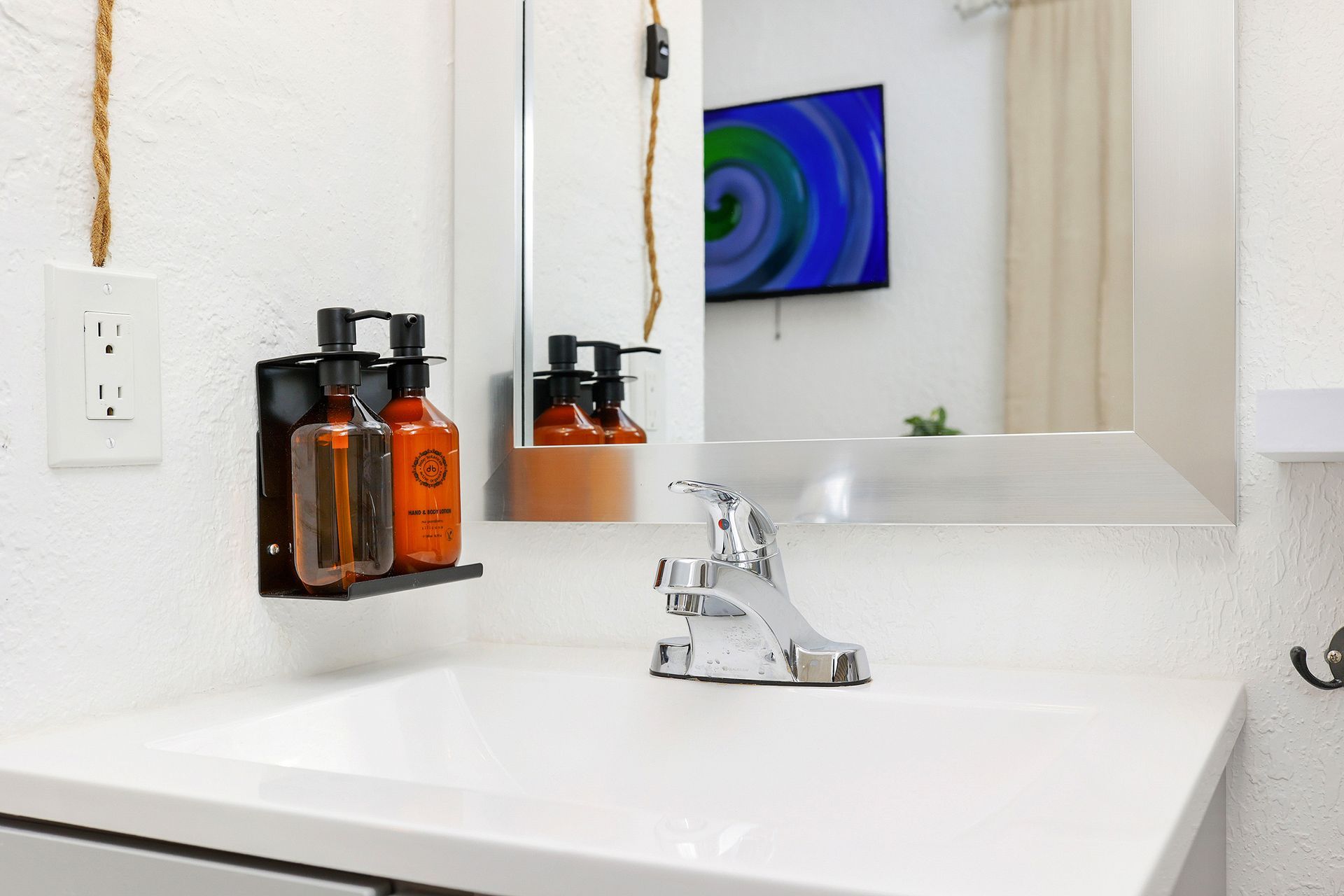 Bathroom sink with a mounted soap dispenser and mirror; a television is visible in the background.
