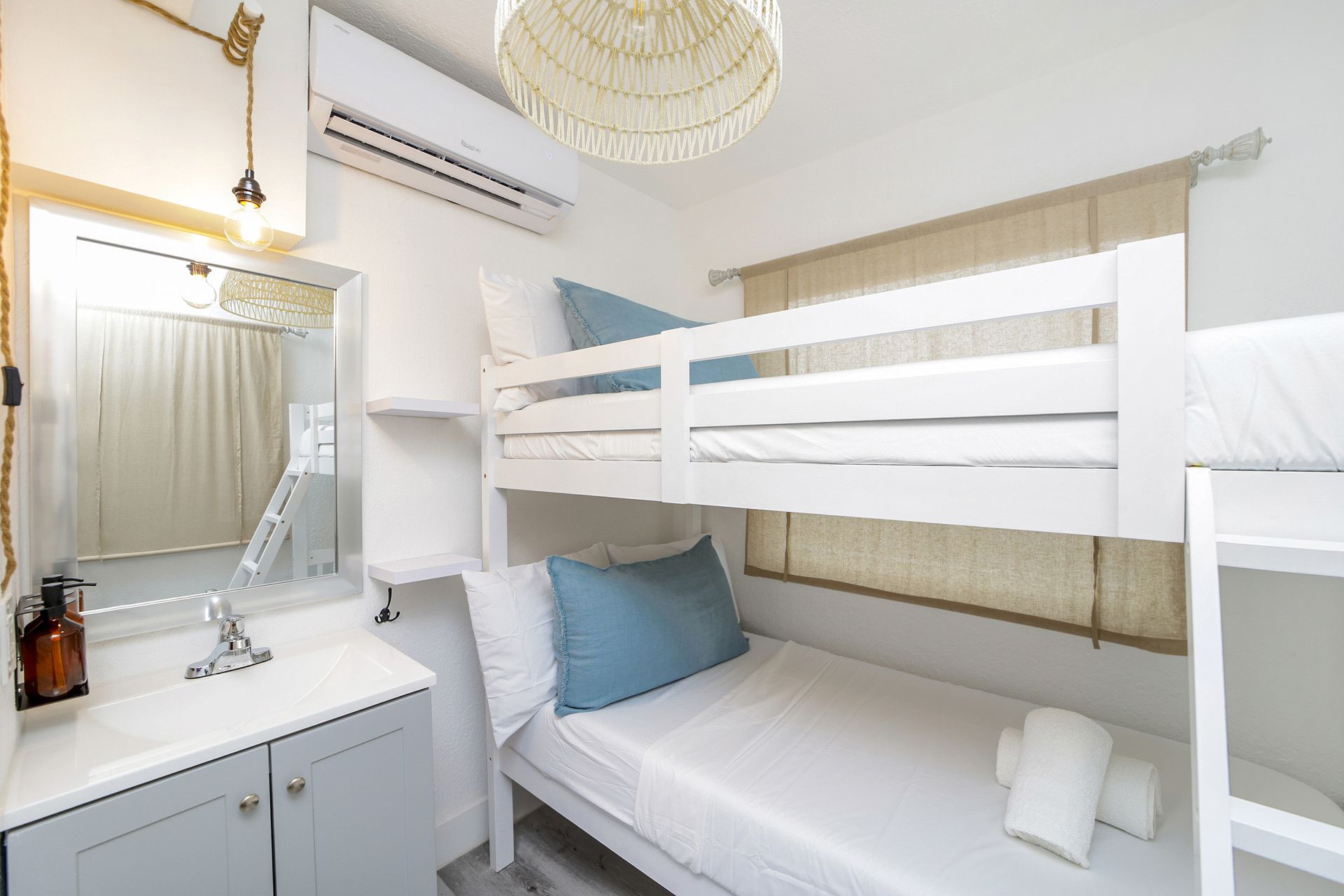 White bunk beds in a bright room with a sink and a mirror.