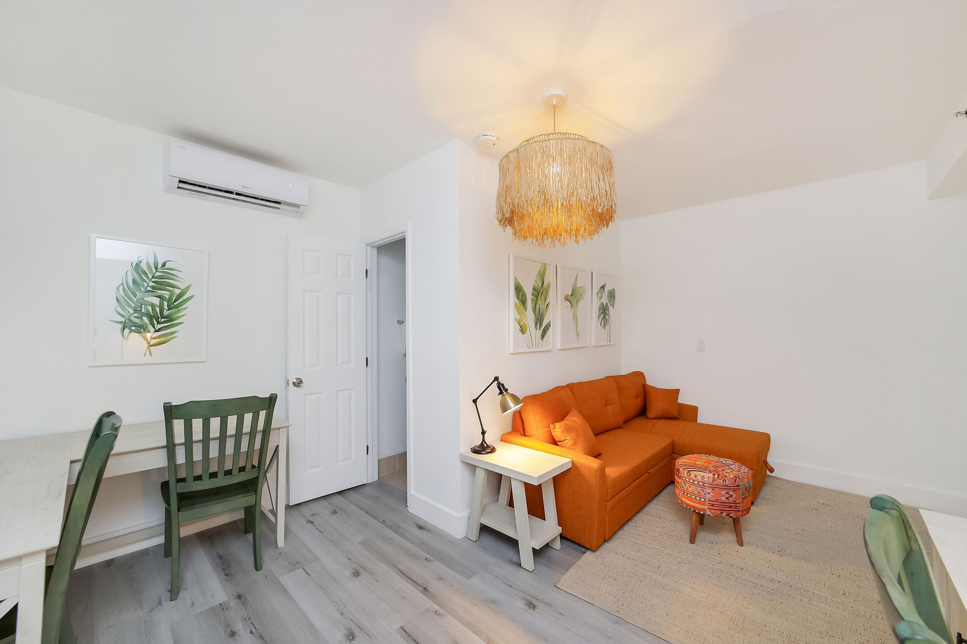 Bright living space with an orange sectional sofa, small desk, and light wood flooring.