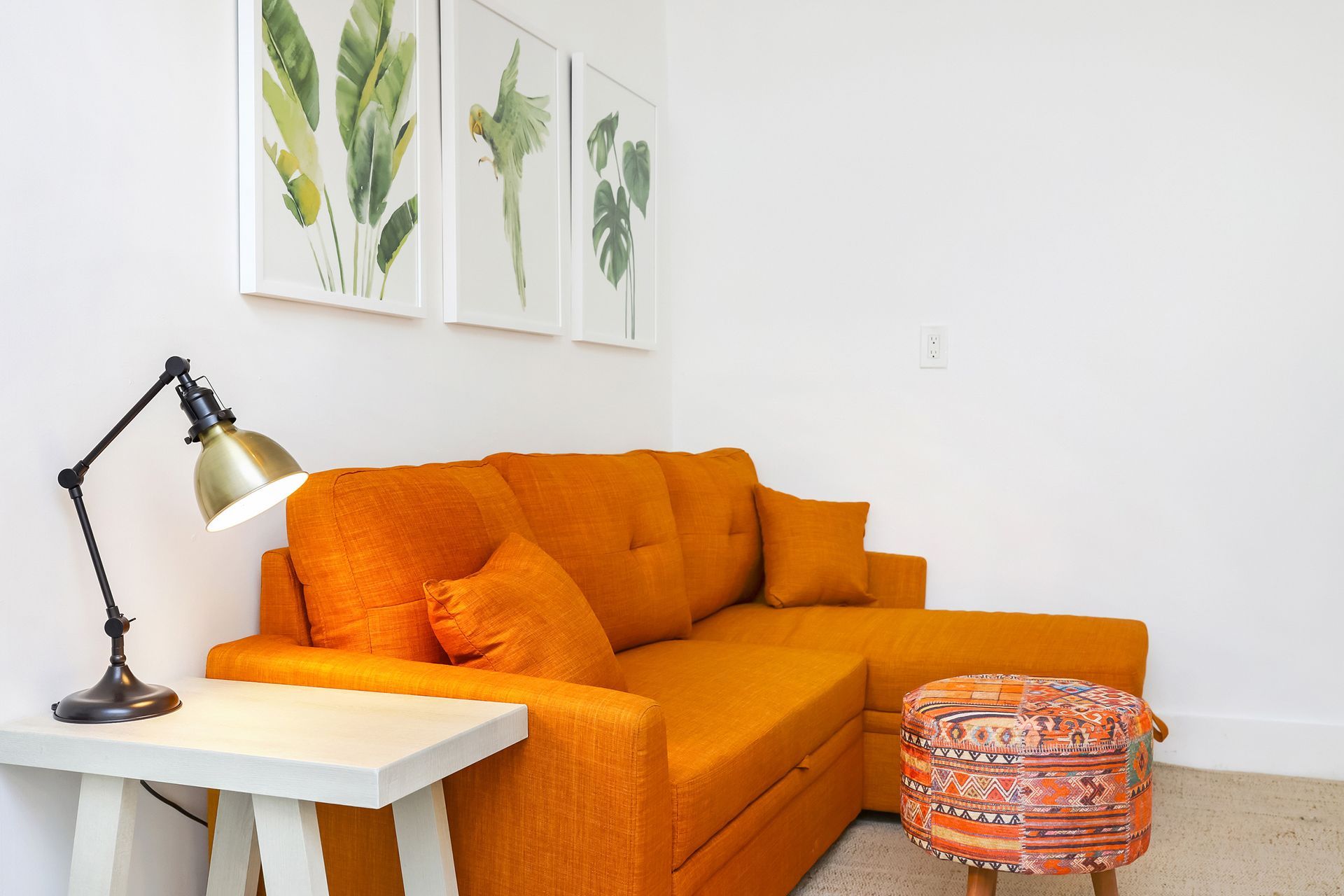Orange sectional sofa in a room with white walls, a side table with a lamp, and botanical art prints.