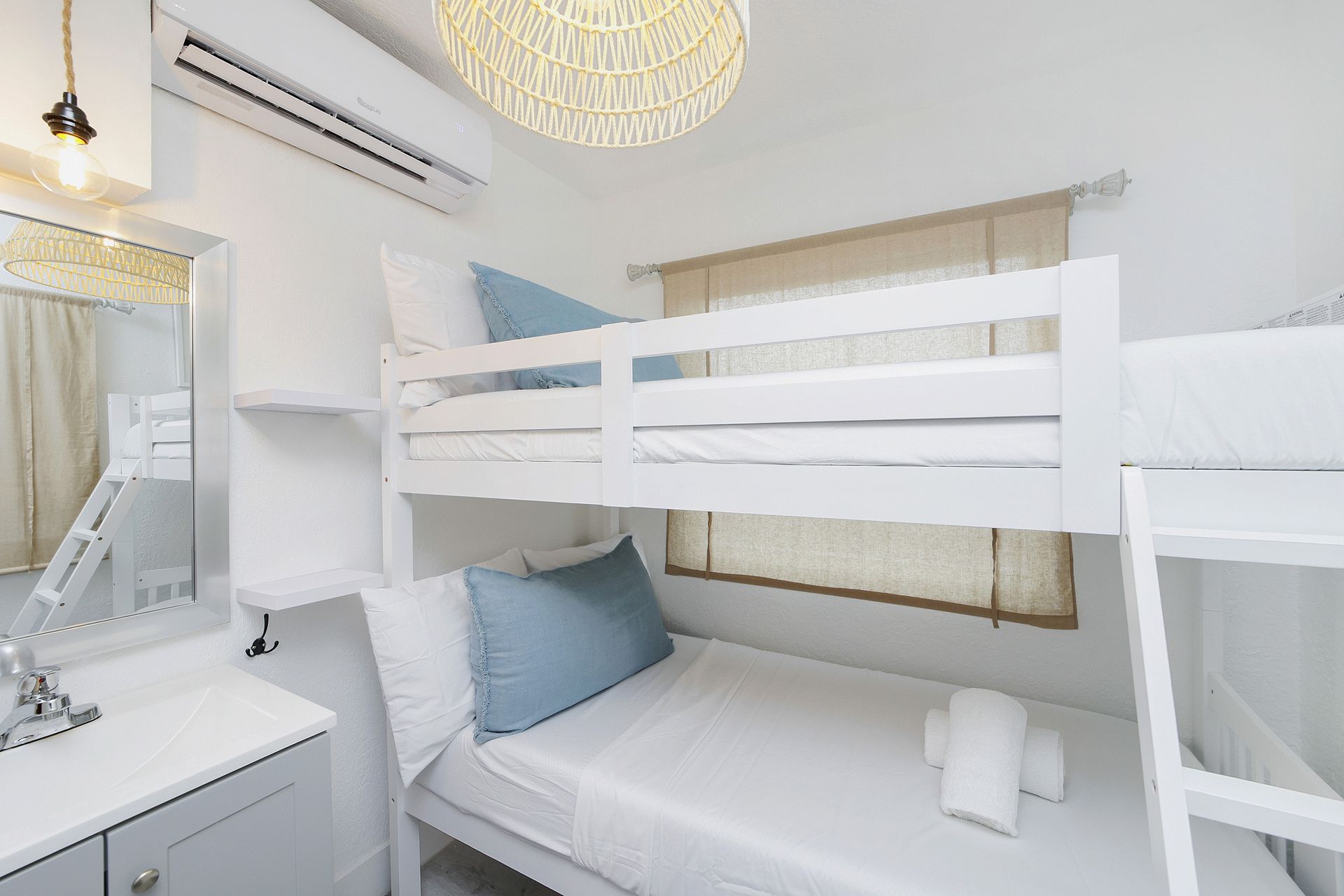 A small bedroom with white bunk beds, a vanity, and an air conditioner.