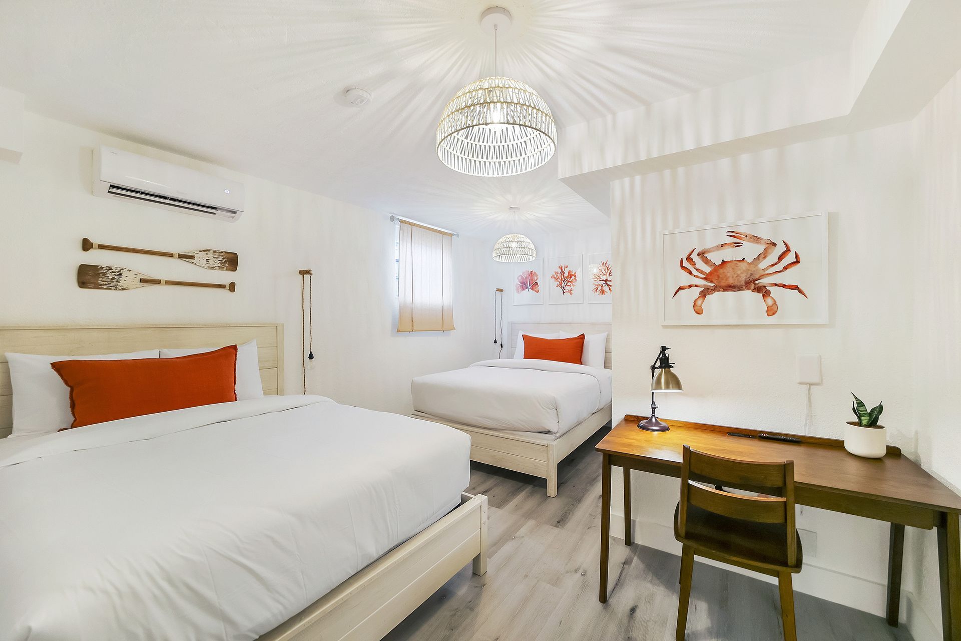 White bedroom with two beds, red accents, desk, and crab artwork.