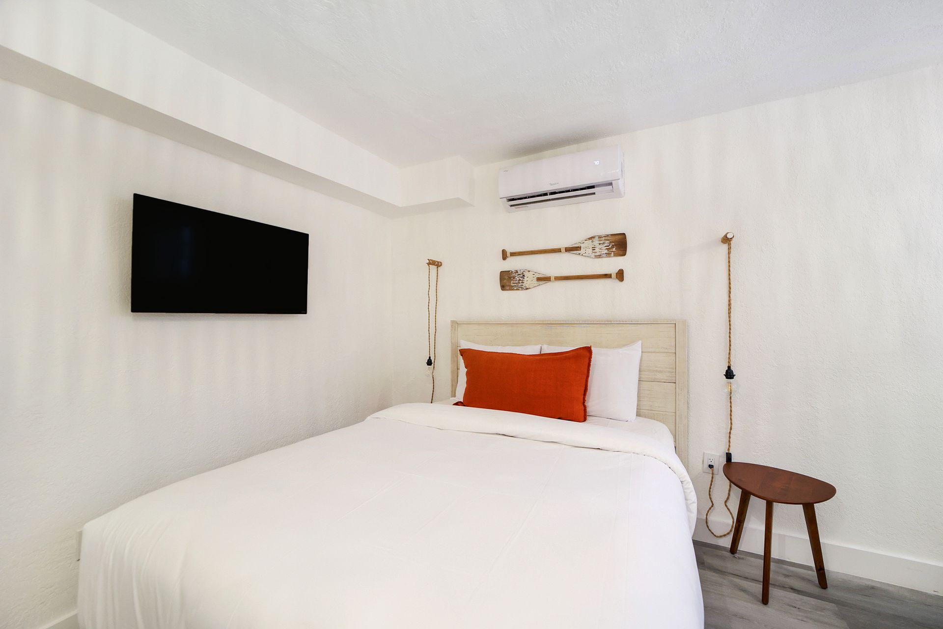 Bedroom with white walls, bed with orange pillow, TV, oars, stool.