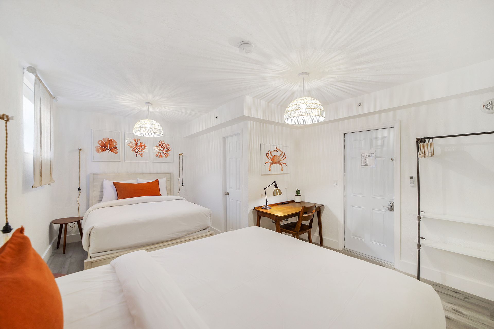 Bright white hotel room with two beds, orange pillows, and decorative lights.