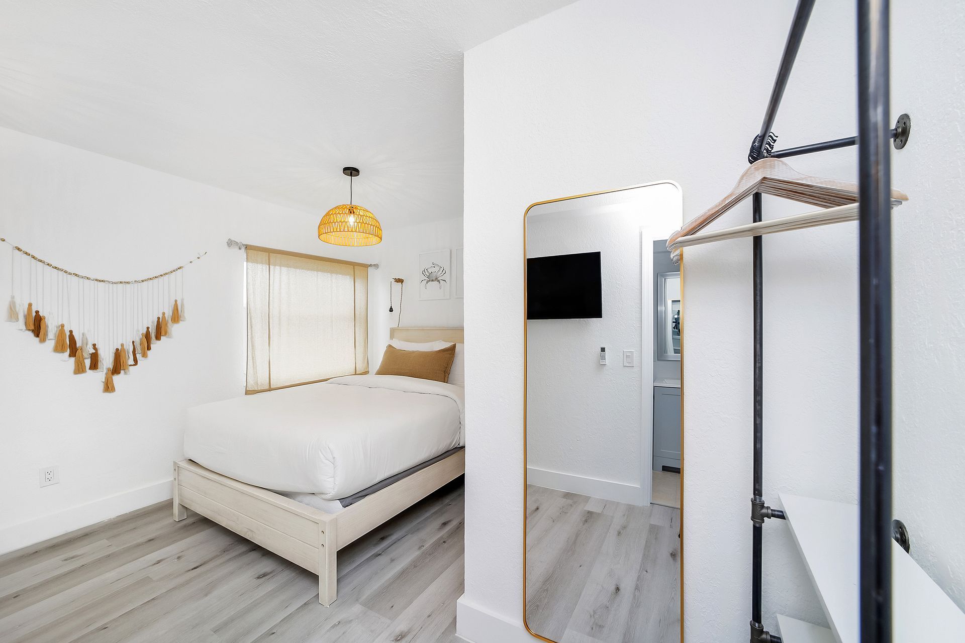 Bedroom with a white bed, beige decor, full-length mirror, TV, and black clothing rack.