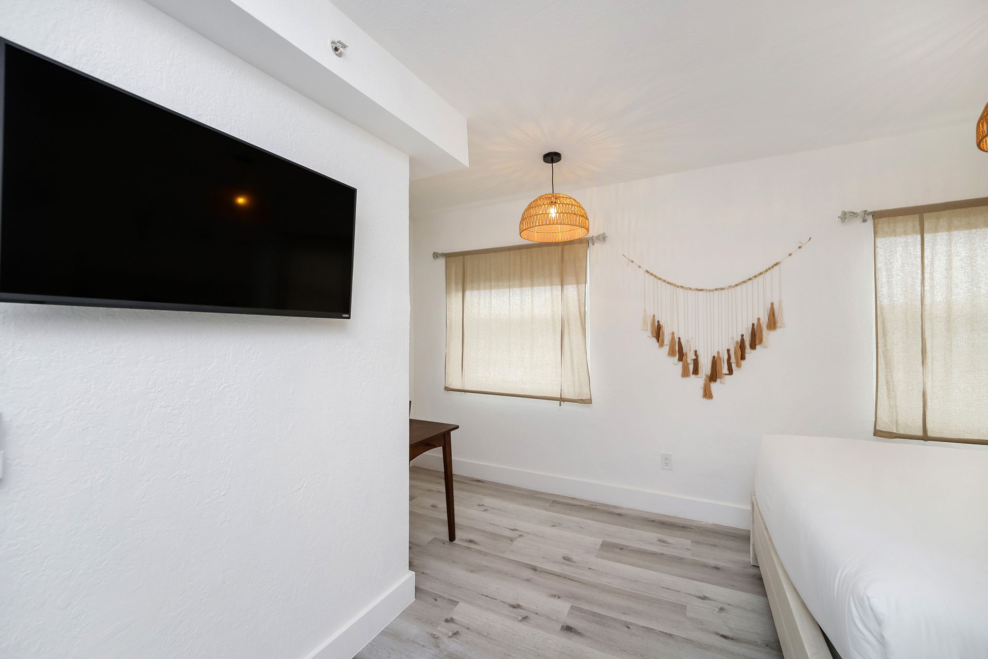 Interior of a bright bedroom with a bed, TV, desk, and neutral decor.