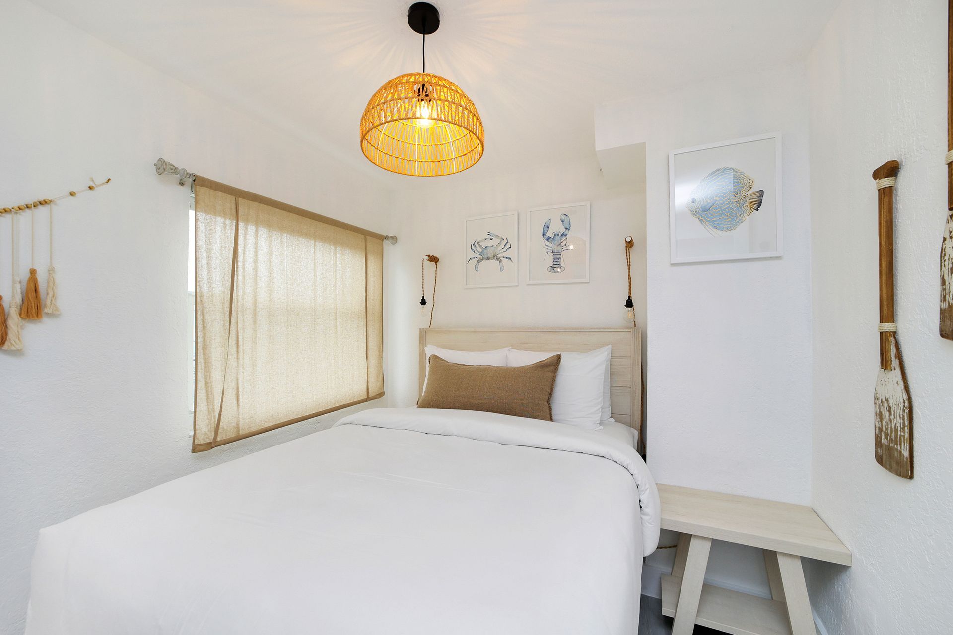 White bedroom with a single bed, woven pendant light, small window, and coastal decor.