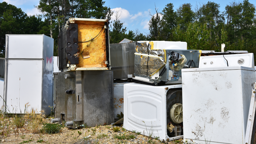 Scattered discarded appliances and scrap metal in an outdoor junkyard under a blue sky