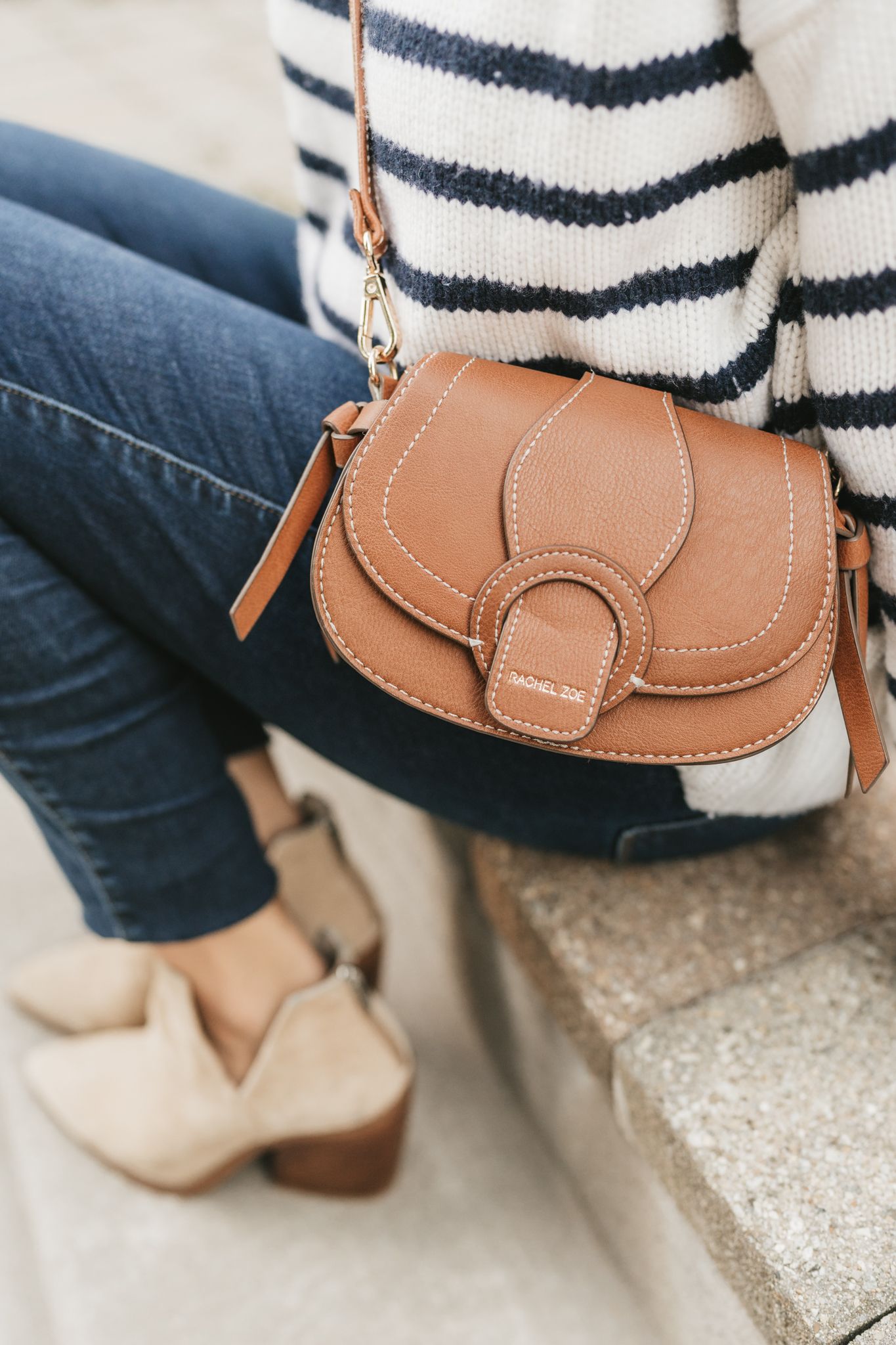 A woman wearing a striped sweater and jeans is holding a brown purse.