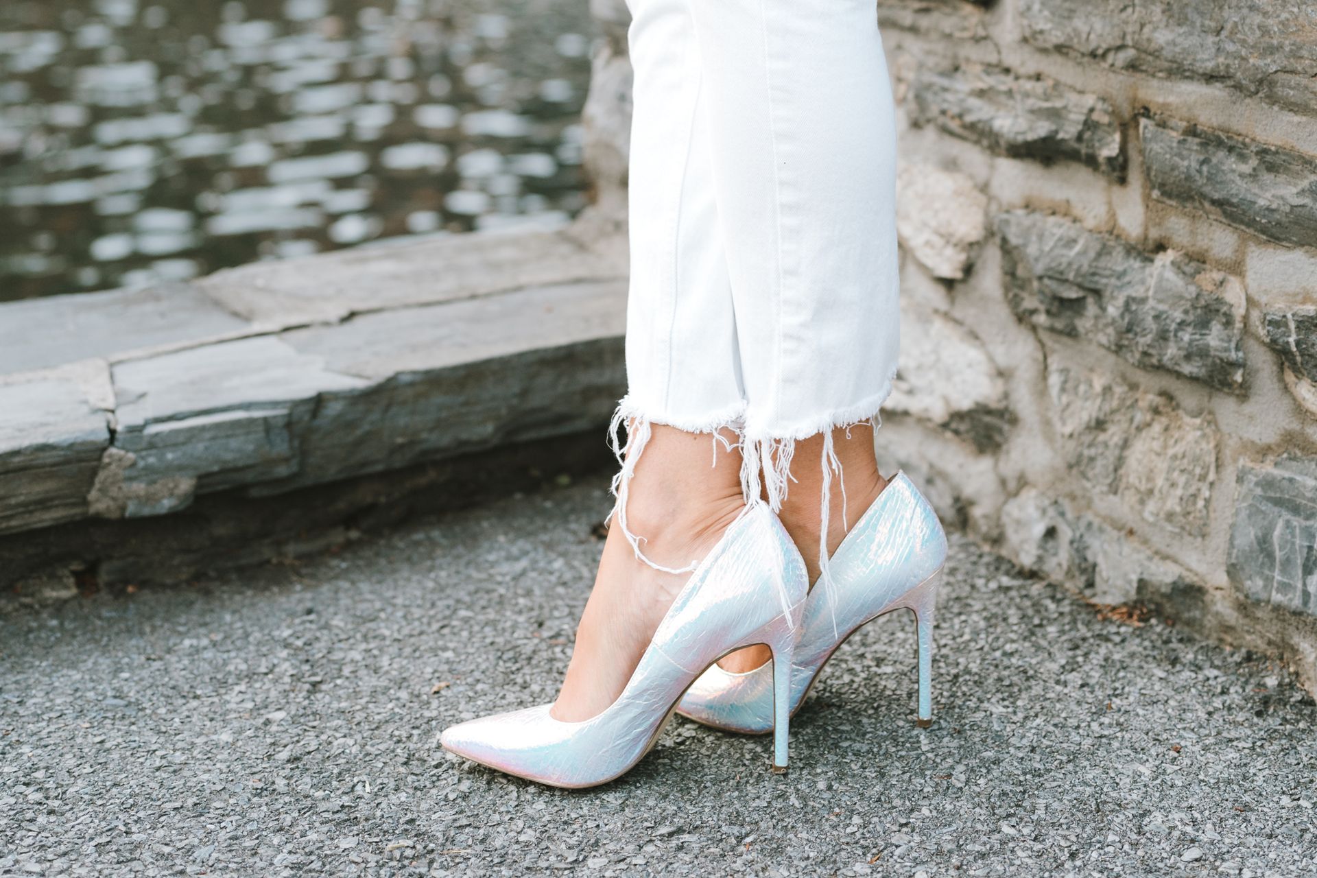 A woman wearing white high heels is standing next to a stone wall.
