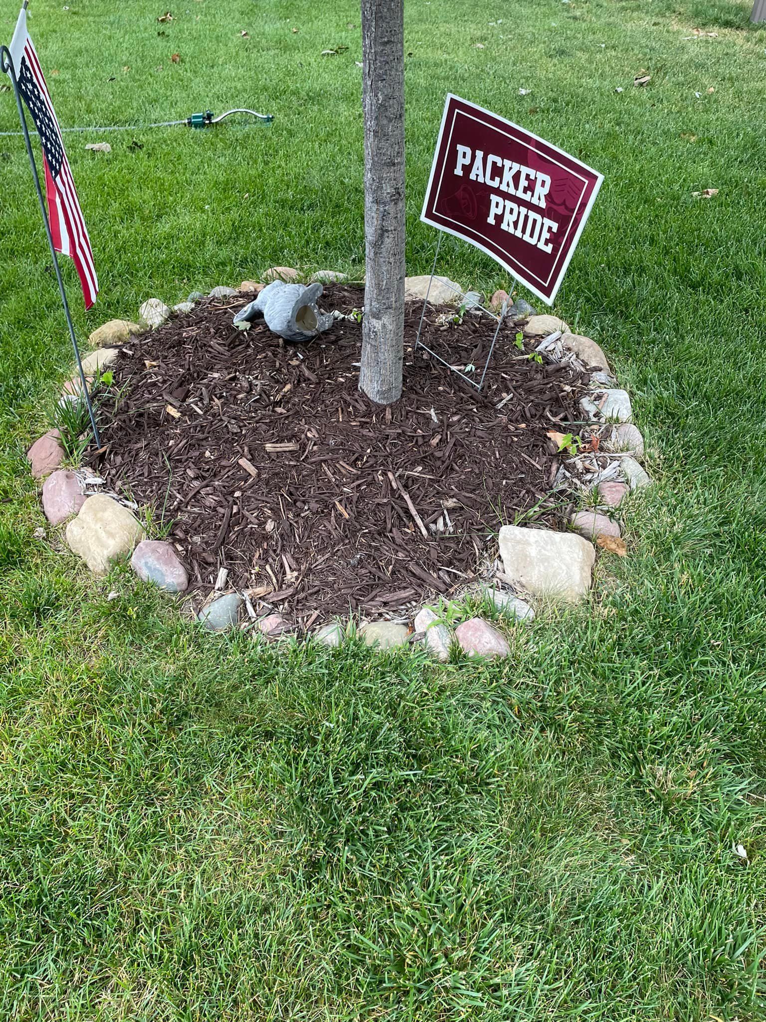 A tree surrounded by mulch and a border of stones, featuring a maroon 