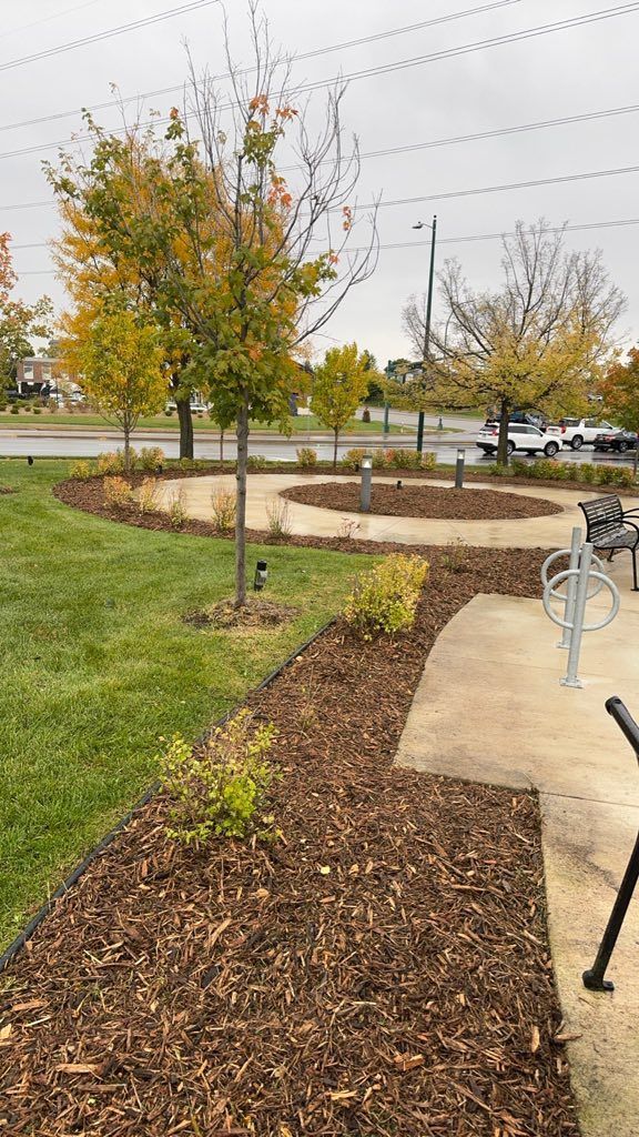 A landscape view of trees and shrubs planted in mulch beds alongside a concrete path with a bike rack.