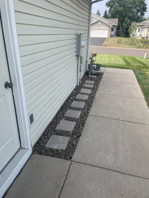 Side yard with concrete walkway and mulch bed lined with stepping stones beside a white house.