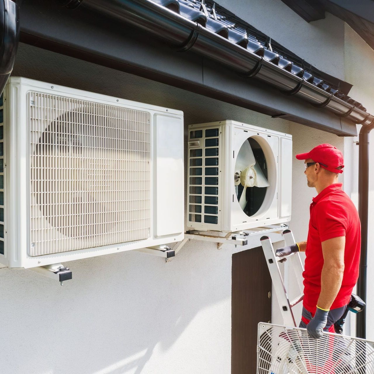 HVAC technician in red shirt servicing AC units outside a building, holding a tool.