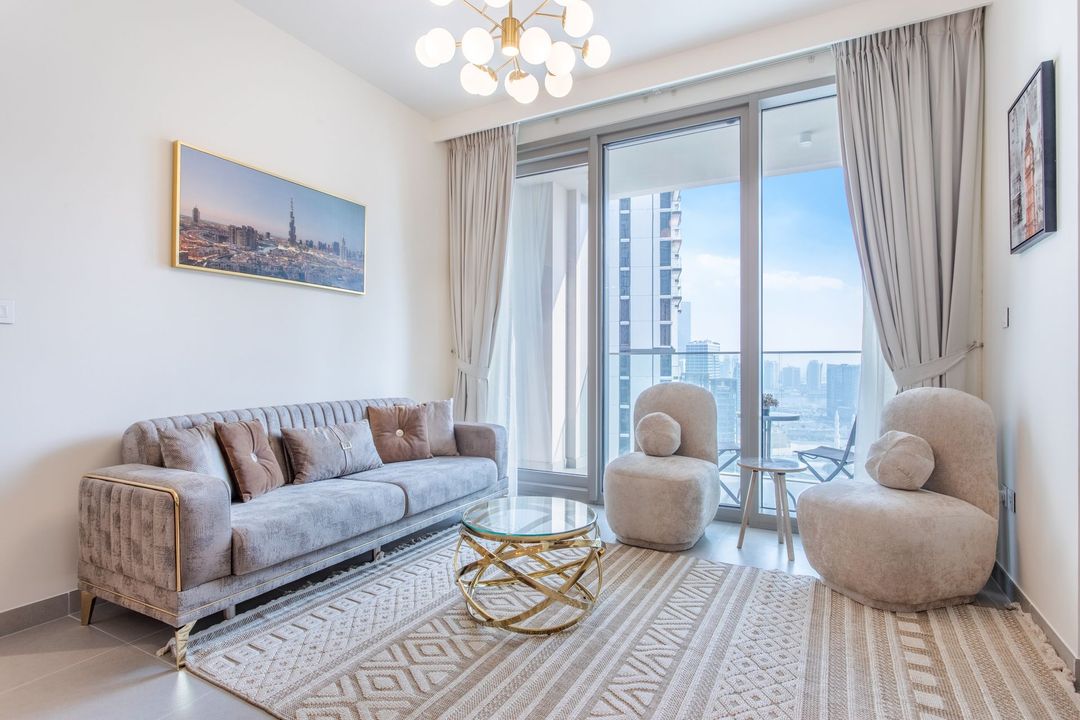 Elegant living room with beige sofa, coffee table, and floor-to-ceiling windows overlooking a city skyline.