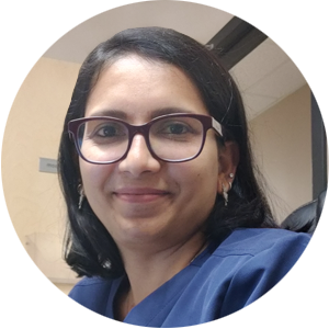 A woman wearing glasses and a blue scrub smiles for the camera