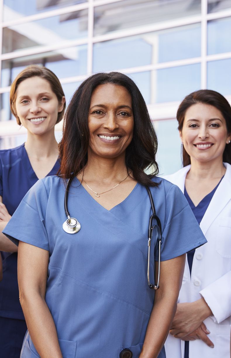 A group of female doctors and nurses are posing for a picture in front of a hospital.