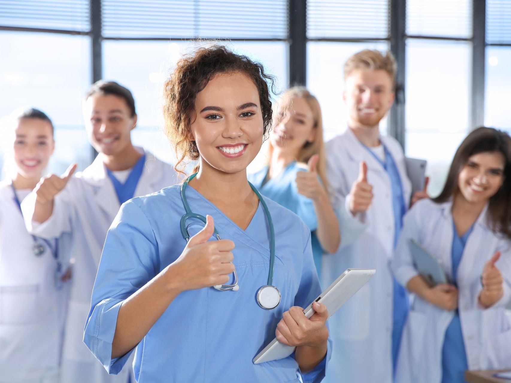 A group of doctors and nurses are giving a thumbs up in a hospital.