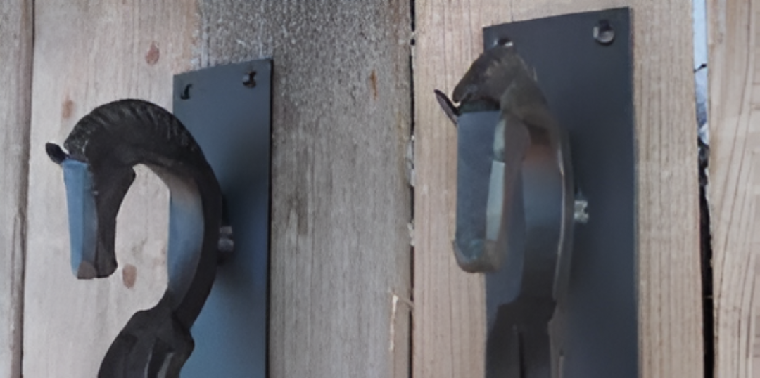 Dos tiradores de puerta con forma de cabeza de caballo de metal negro montados en una puerta de madera.