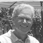 A man wearing glasses is smiling in a black and white photo.