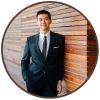A man in a suit and tie is standing in front of a wooden wall.
