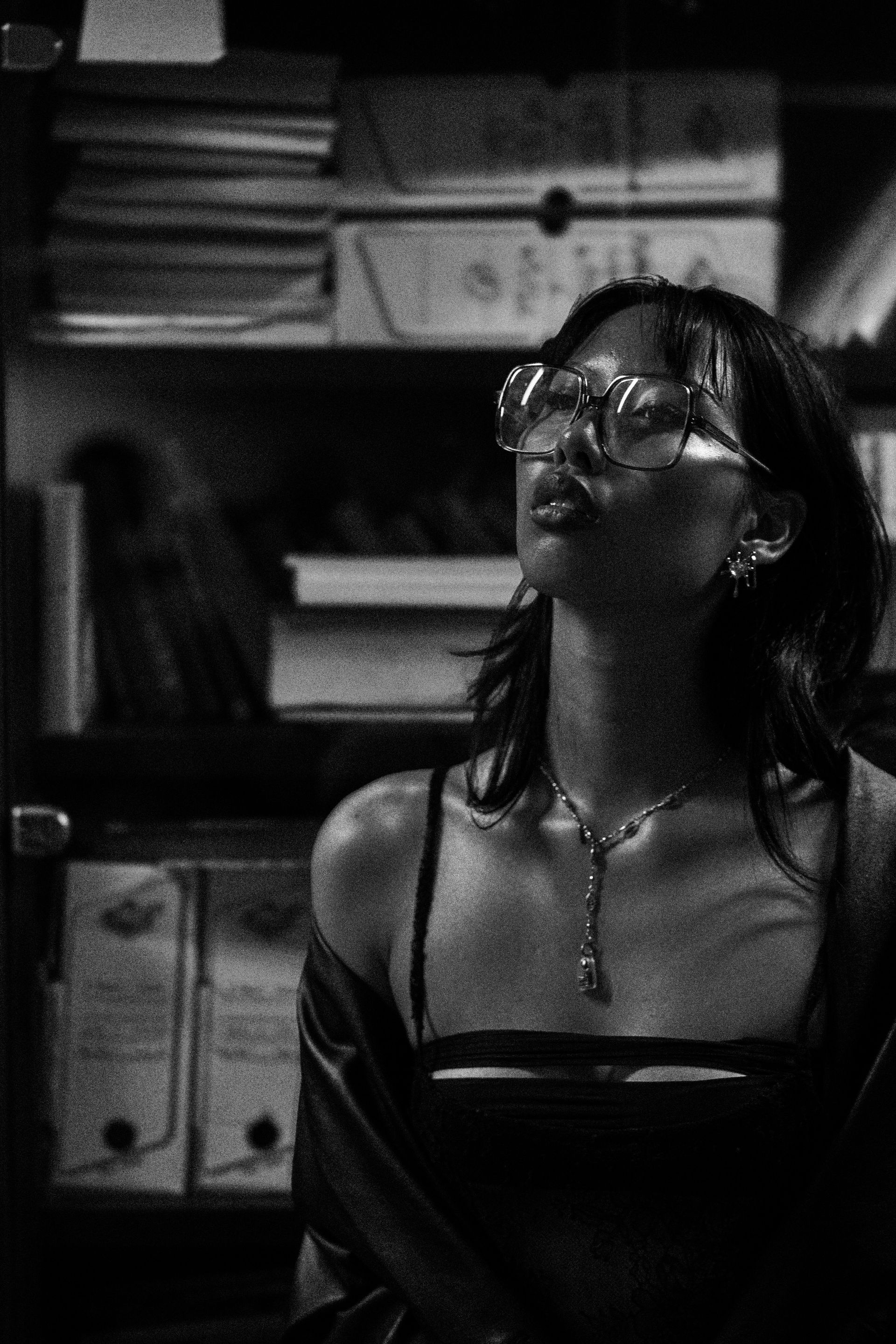 Femme portant des lunettes, regardant vers le haut, dans une pièce avec une bibliothèque.