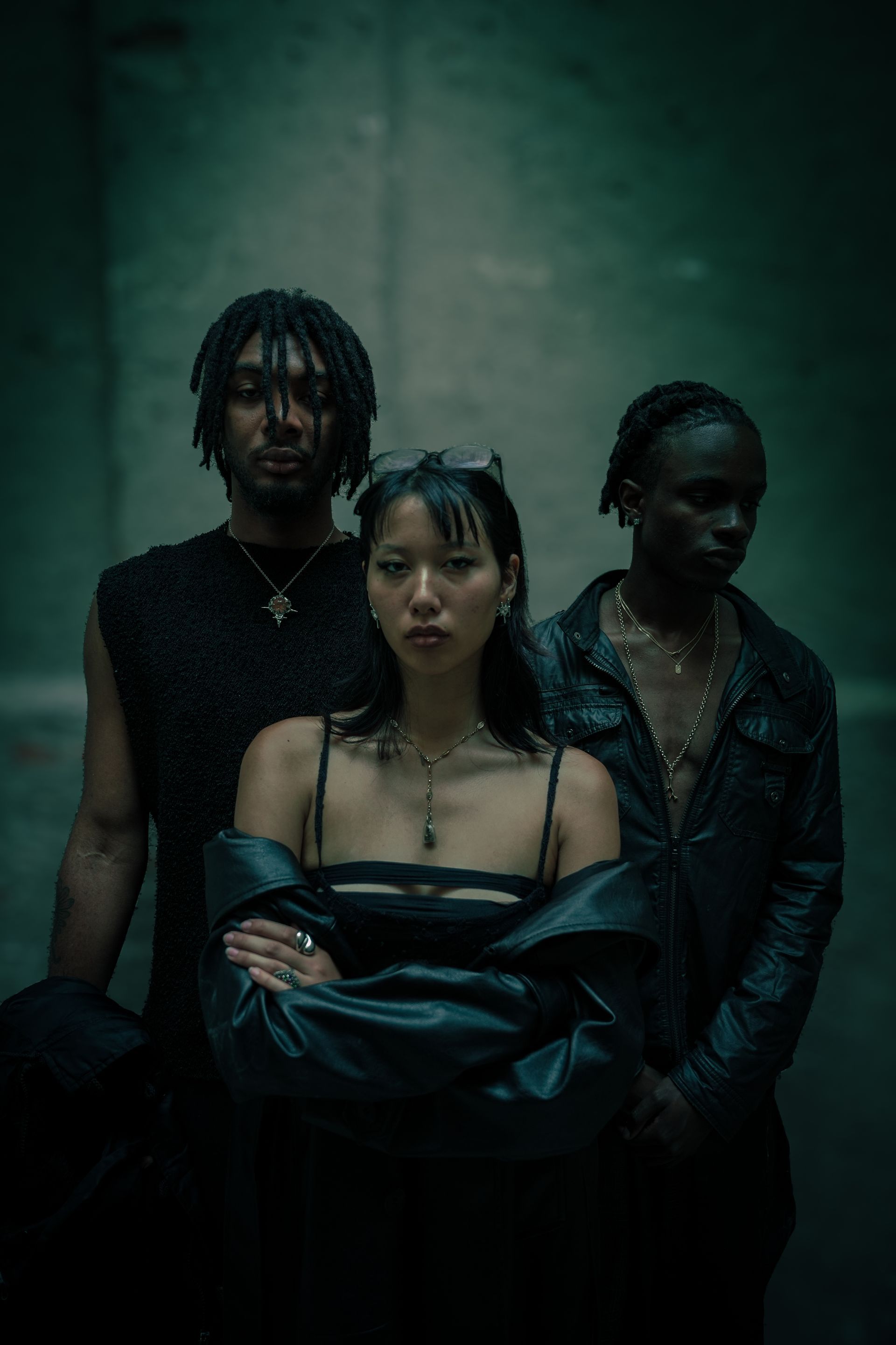 Trois mannequins posent dans un espace faiblement éclairé. Elles portent des vêtements sombres et regardent l'objectif.