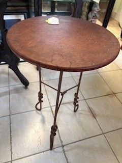Round wooden table with three wrought iron legs, set on tiled floor.