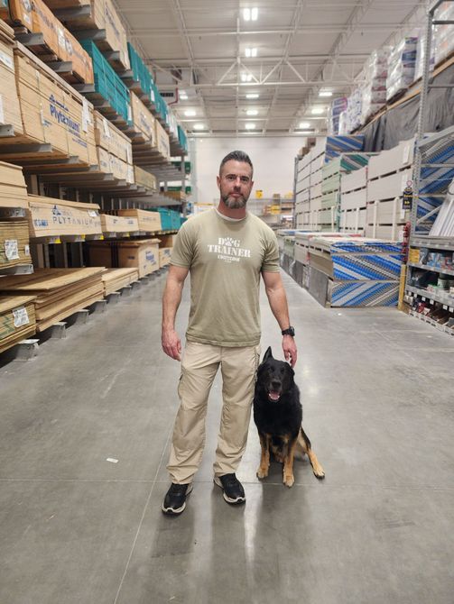 Man in beige pants and t-shirt with a black and tan dog in a hardware store.
