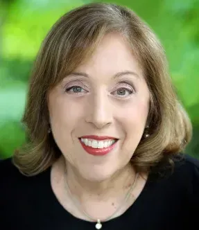 A woman wearing a black shirt and a necklace is smiling for the camera.