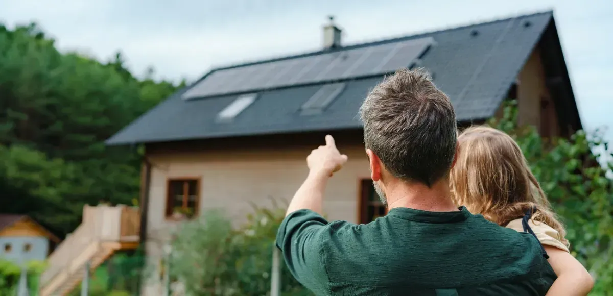 A man and a child are looking at a house with solar panels on the roof.