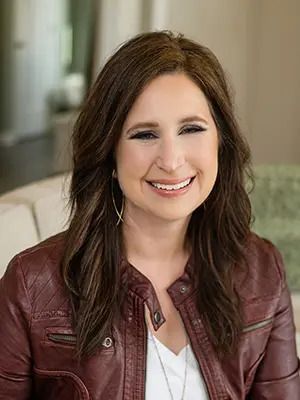 Smiling woman in a maroon jacket standing indoors against a softly blurred background