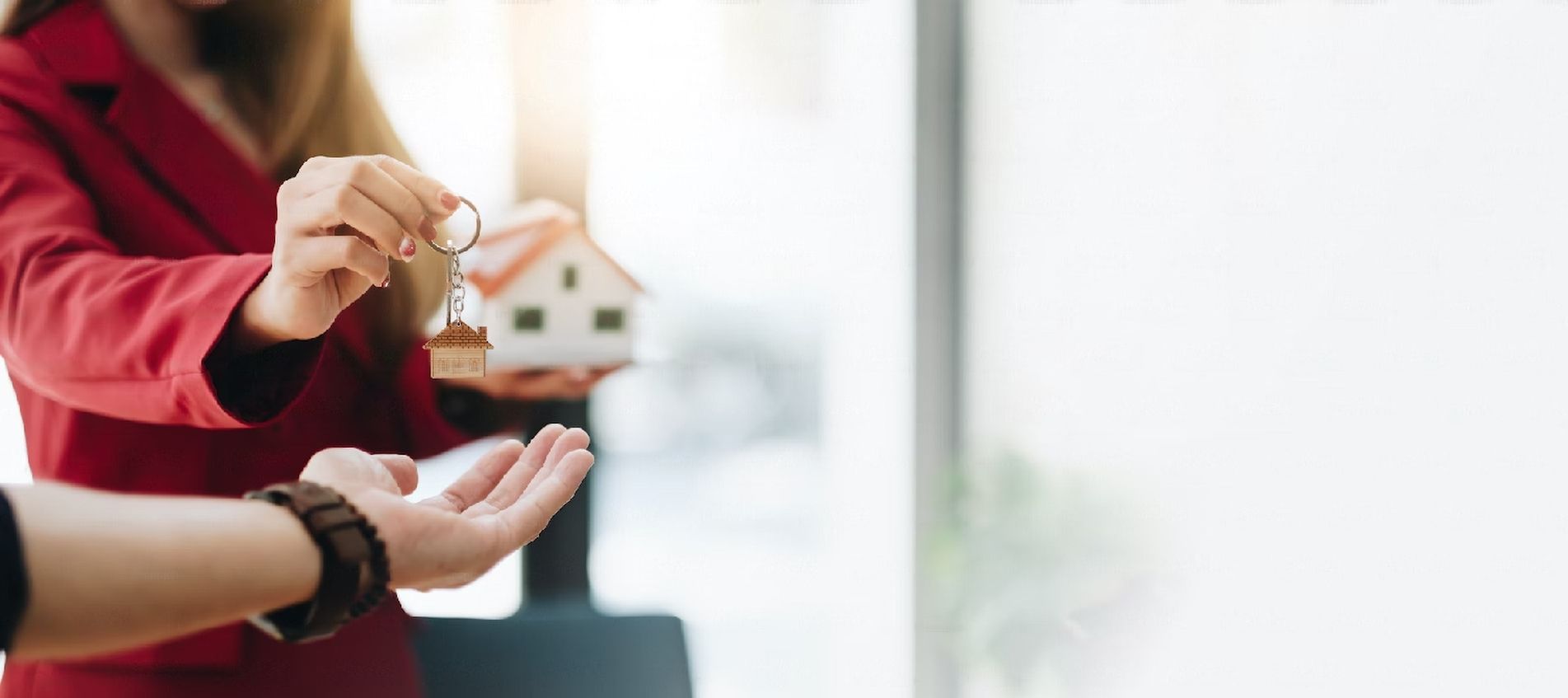 A woman is giving a key to a man while holding a model house.