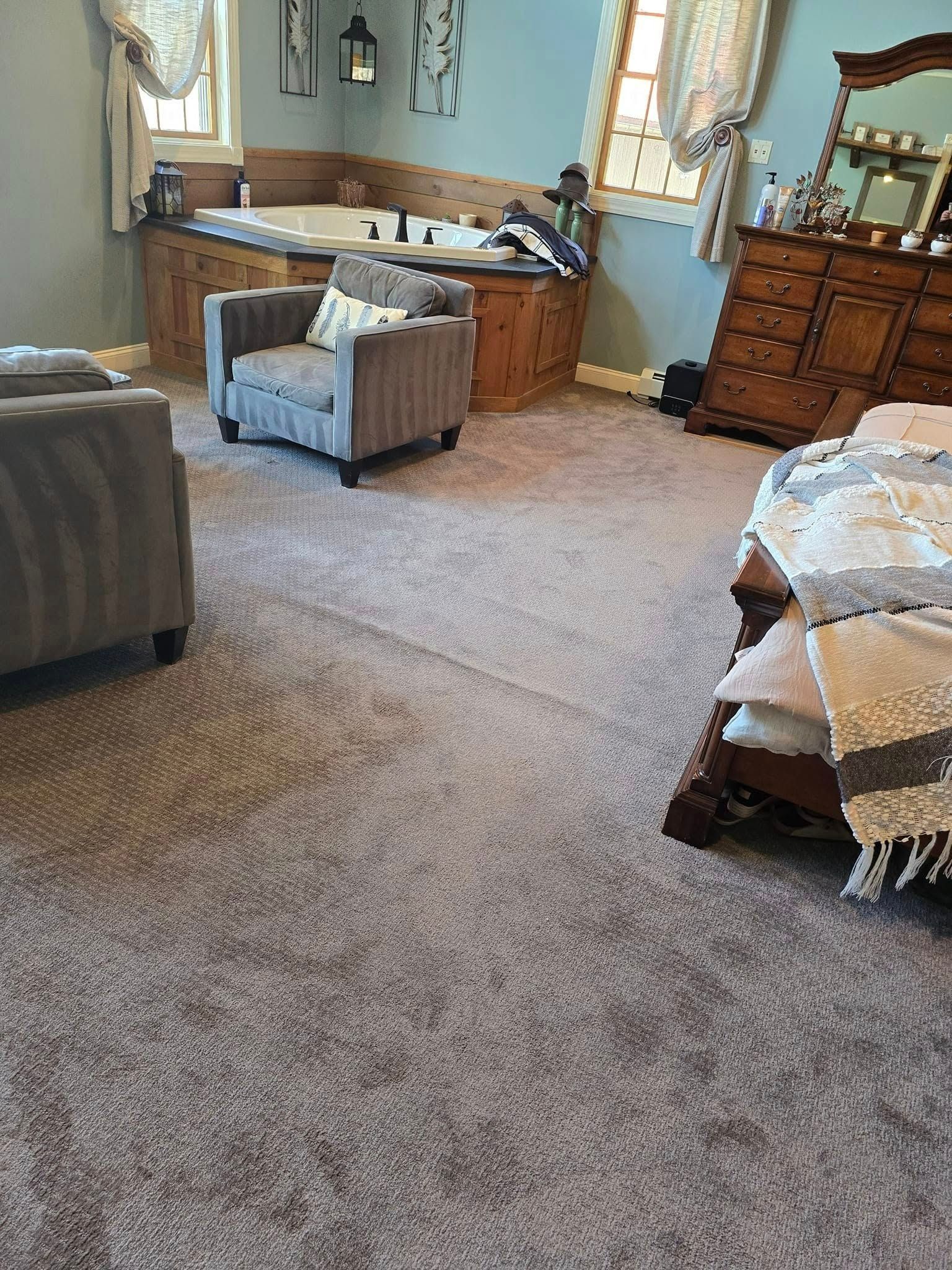 A bedroom featuring carpeted flooring, a gray armchair, a large wooden dresser with a mirror, and a built-in bathtub.