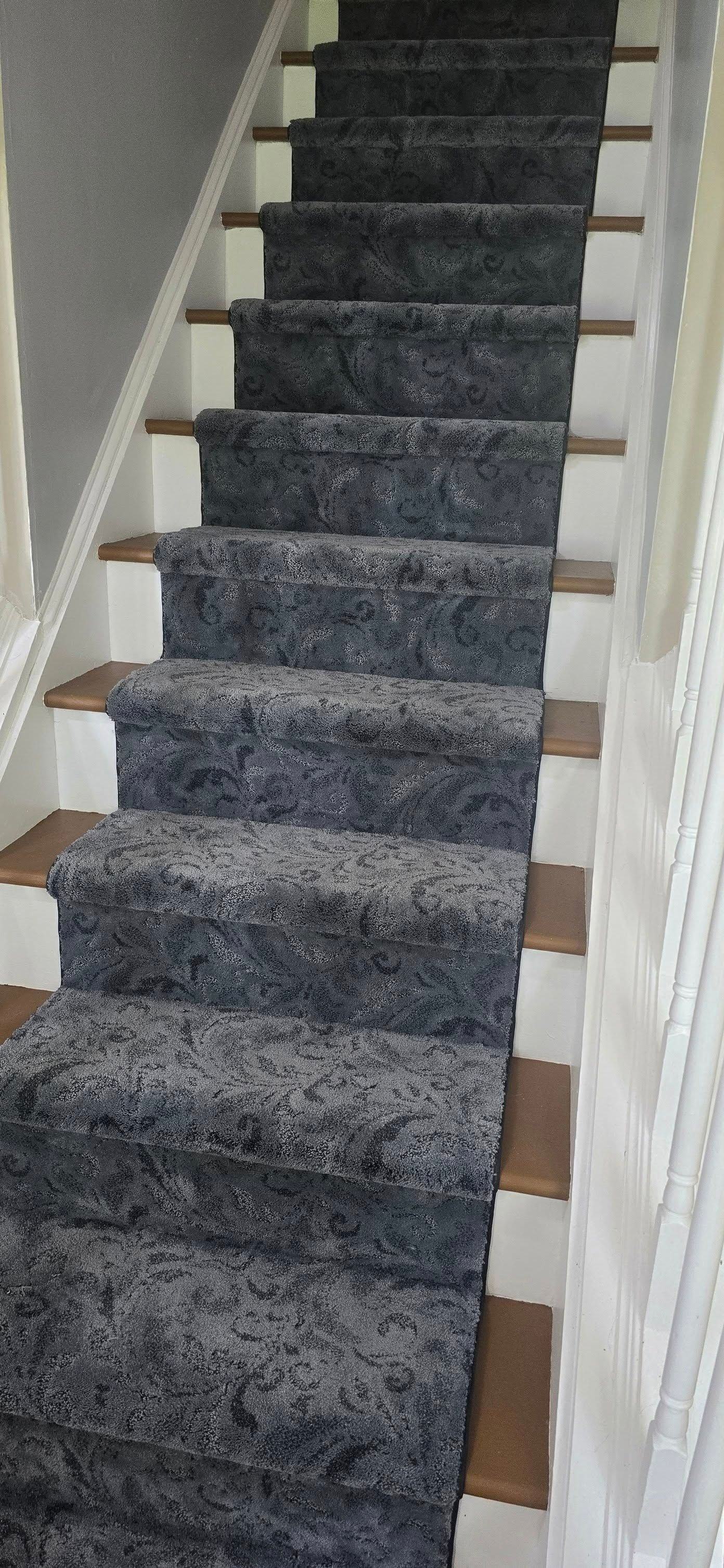 A staircase with white sides and wooden step edges, covered by a grey, textured carpet runner.