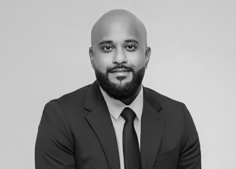 Man in a suit, bald with a beard, smiling, looking at the camera.
