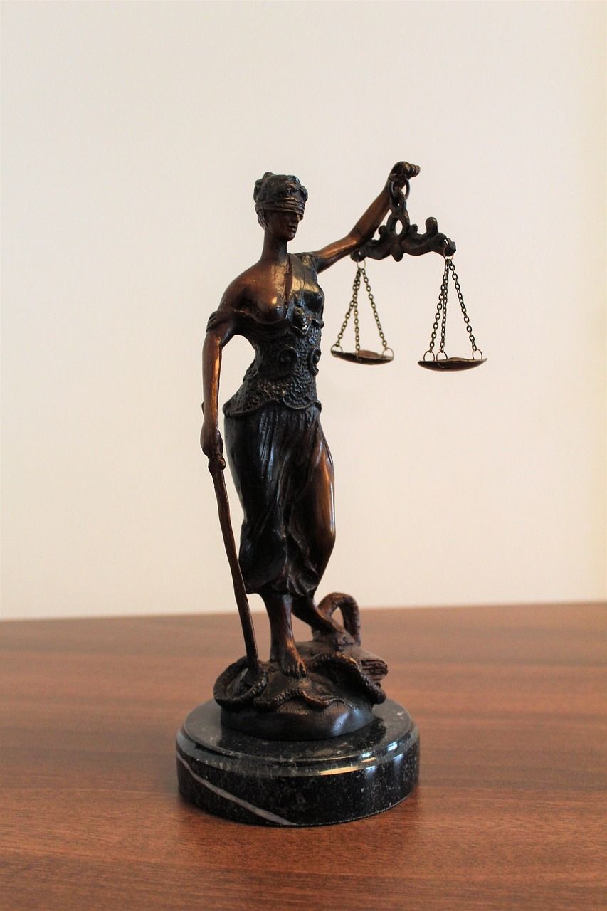 Statue of Lady Justice holding scales and a sword, bronze-colored on a marble base.